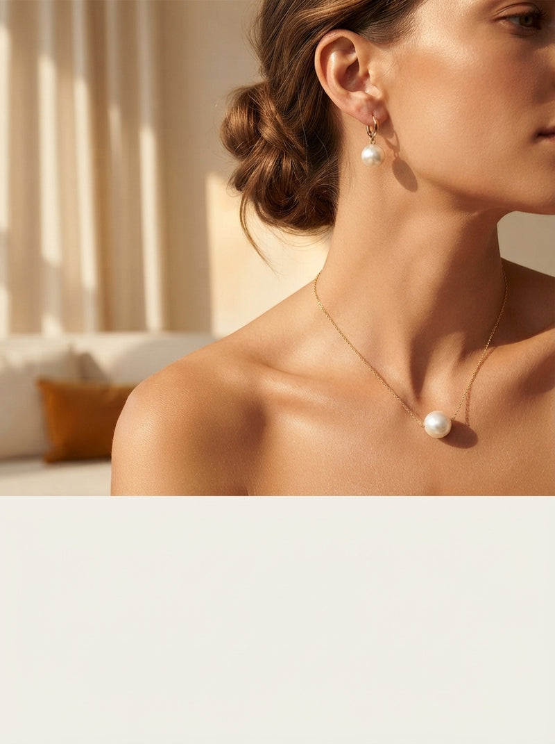 A woman wearing a pearl necklace and earrings in a sunlit, elegant room with soft cream and amber tones.